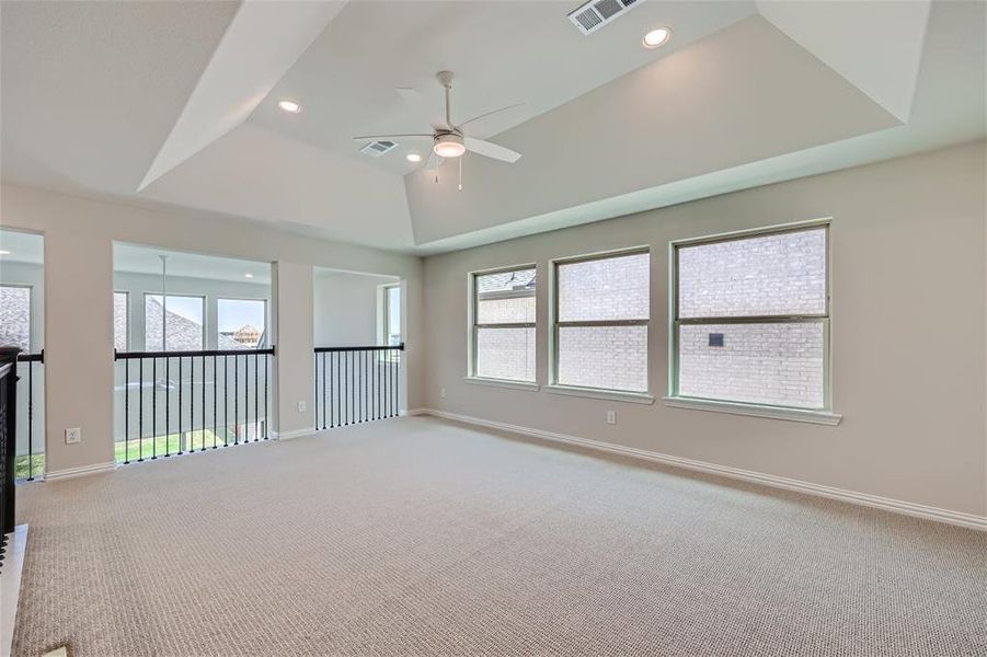 Carpeted spare room with plenty of natural light, ceiling fan, and a raised ceiling