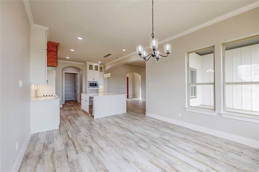 Kitchen featuring hanging light fixtures, stainless steel microwave, white cabinetry, light hardwood / wood-style flooring, and crown molding