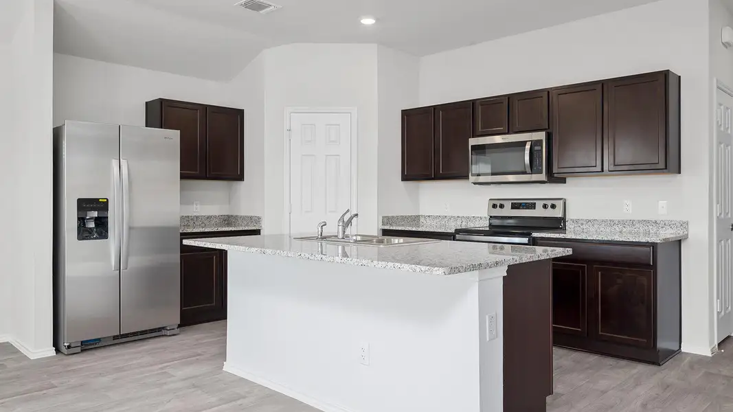 Kitchen featuring appliances with stainless steel finishes, dark brown cabinets, light stone counters, a kitchen island with sink, and light wood-style floors