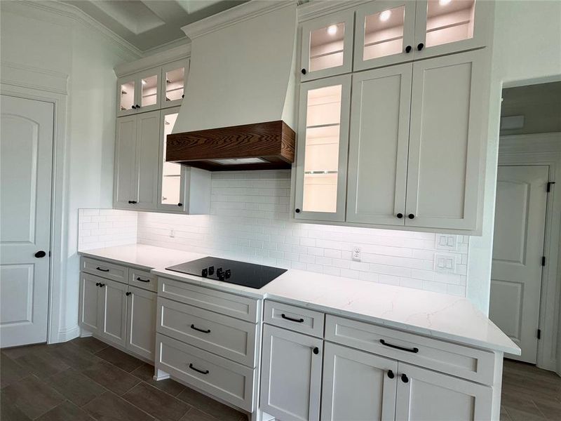 Modern kitchen featuring white shaker cabinetry, quartz countertops, a black cooktop, a wood-accented range hood, and subway tile backsplash