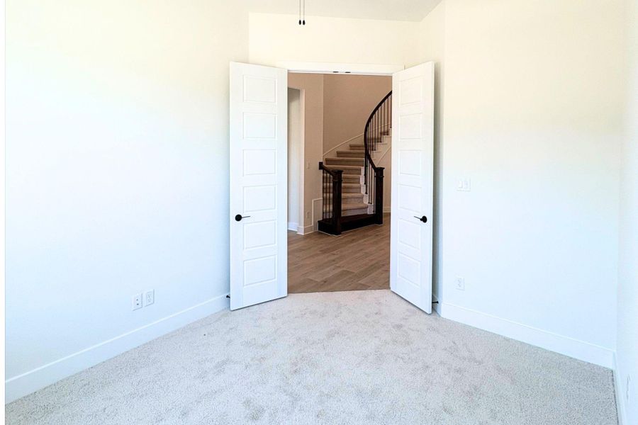 Double doors open to carpeted flooring, leading directly toward a curved staircase. Double doors open to carpeted flooring, leading directly toward a curved staircase.