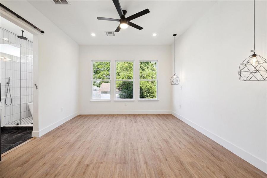 The primary bedroom features barn doors, ceiling fan, recessed lighting, pendant lighting, large windows, and an en-suite bathroom, and hanging pendant lights for nightstands.