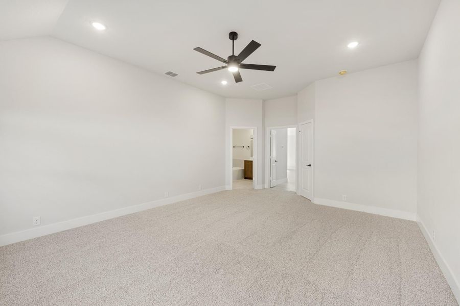 Empty bedroom with beige carpet, black ceiling fan, and doorway leading to an ensuite bathroom