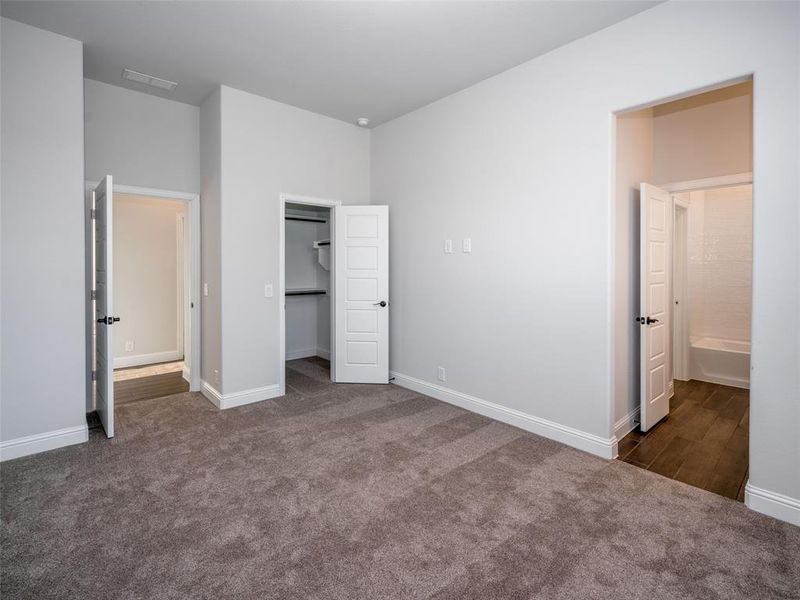 Unfurnished bedroom with dark colored carpet, a walk in closet, and ensuite bathroom