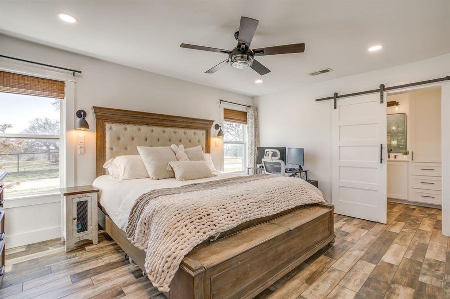 Bedroom with a barn door, light wood-type flooring, a ceiling fan, ensuite bathroom, and recessed lighting