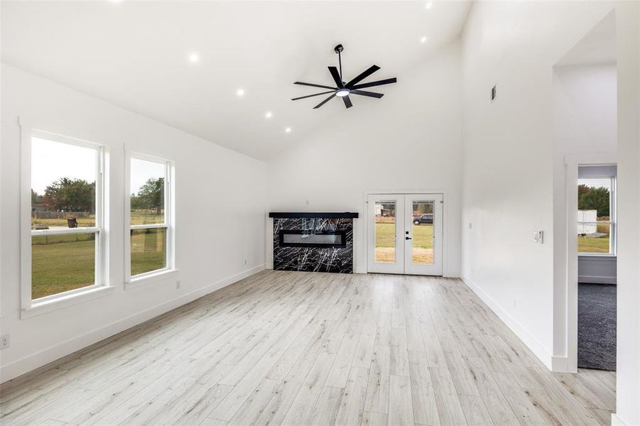 Unfurnished living room featuring high vaulted ceiling, recessed lighting, light wood finished floors, french doors, and ceiling fan Unfurnished living room featuring high vaulted ceiling, recessed lighting, light wood finished floors, french doors, and ceiling fan