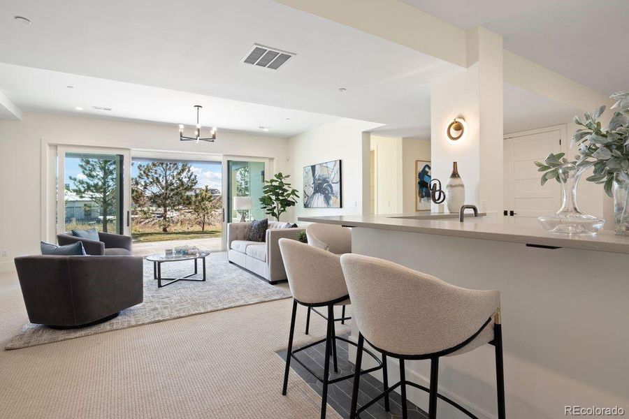 Another view of the open-concept lower level with walk-out access, a wet bar, bright Level-5 finished walls and plush carpeting.