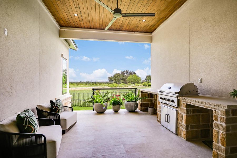 An inviting outdoor patio features an integrated kitchen and serene countryside views.