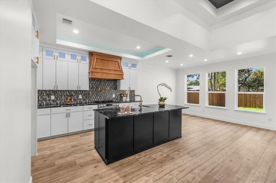 Kitchen featuring a tray ceiling, white cabinetry, backsplash, a kitchen island with sink, and recessed lighting
