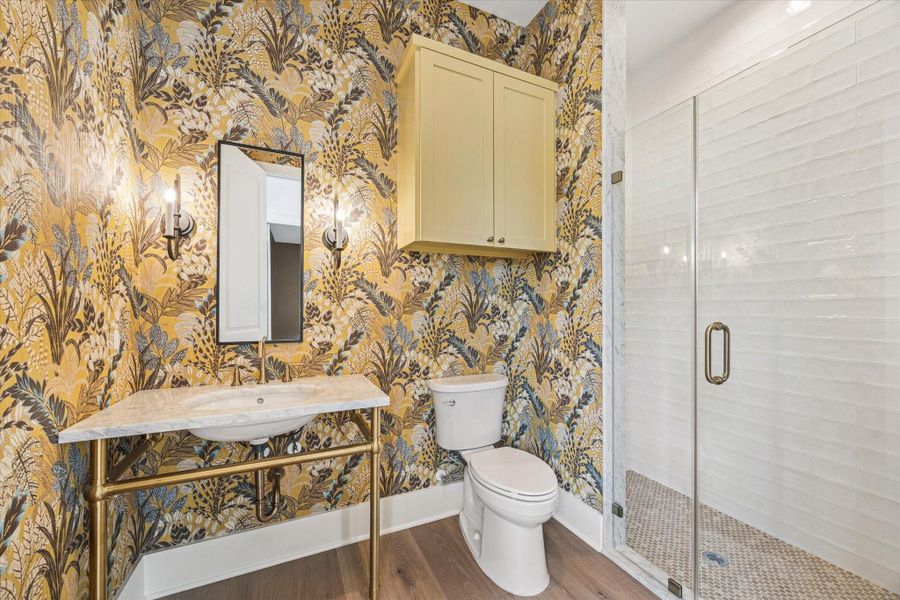 Bold botanical wallpaper and a marble topped console vanity wrapped in brass create a powder bath that feels like a designer moment. Framed glass shower with marble trim and penny tile flooring elevates this space well beyond expected for guest quarters.