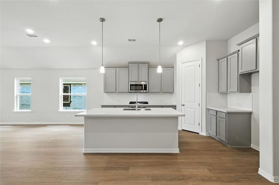 Kitchen with gray cabinetry, decorative backsplash, an island with sink, dark wood-type flooring, and recessed lighting Kitchen with gray cabinetry, decorative backsplash, an island with sink, dark wood-type flooring, and recessed lighting