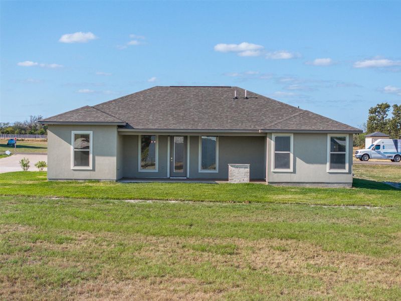 Back of house with a lawn, a shingled roof, and stucco siding