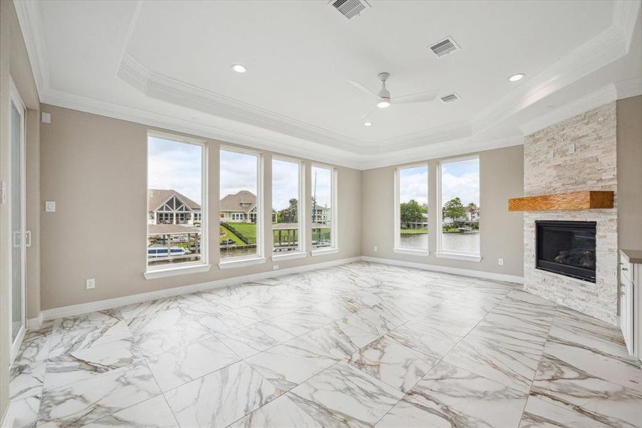 This is an elegant, spacious living area with high ceilings, marble flooring, a modern fireplace, and expansive windows offering abundant natural light and views of a waterway.