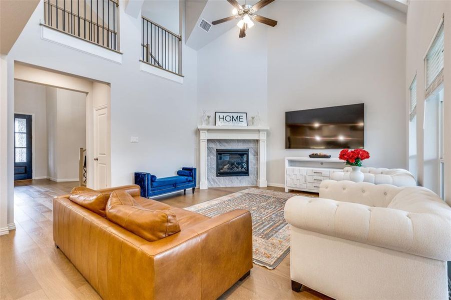 Living room featuring ceiling fan, a fireplace, high vaulted ceiling, and light hardwood / wood-style flooring