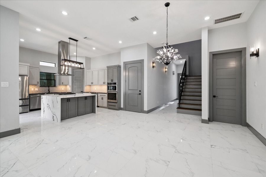A polished look defines the entry, where white tile floors, a statement chandelier, and wall sconces complement an open design leading toward the staircase and main living areas.