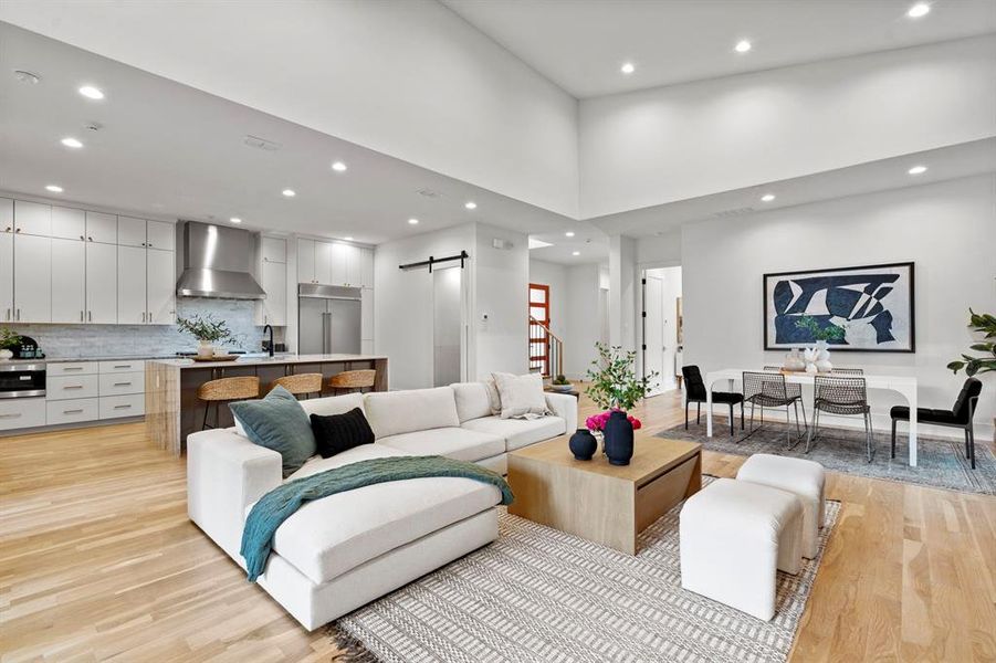 Living room featuring a barn door, light wood-style floors, recessed lighting, and a towering ceiling Living room featuring a barn door, light wood-style floors, recessed lighting, and a towering ceiling