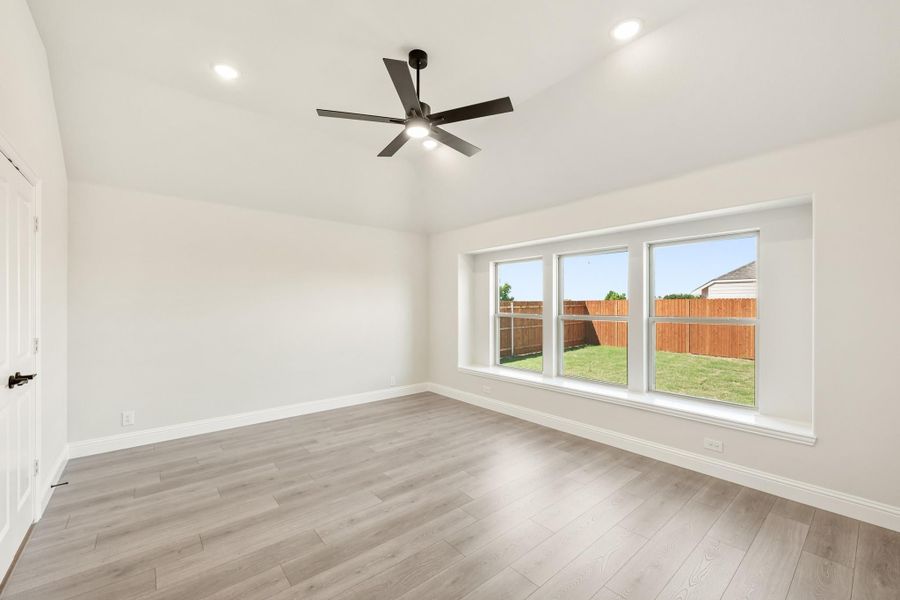 Empty bedroom with light wood floors, ceiling fan, and large windows overlooking fenced backyard Empty bedroom with light wood floors, ceiling fan, and large windows overlooking fenced backyard