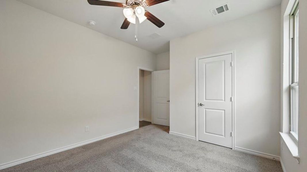 Carpeted room featuring a ceiling fan with light fixture, white interior doors, and a window with white trim