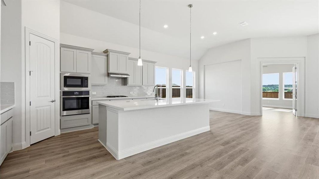 Kitchen featuring a large island with a countertop, gray cabinetry, stainless steel appliances, and wood-finish flooring