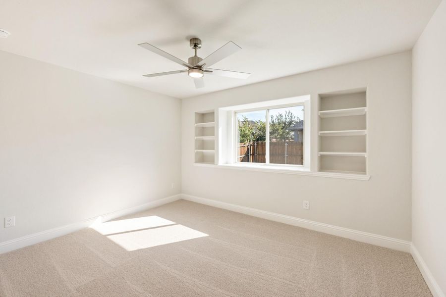 Empty bedroom with carpet, ceiling fan, and built-in shelves flanking a center window Empty bedroom with carpet, ceiling fan, and built-in shelves flanking a center window