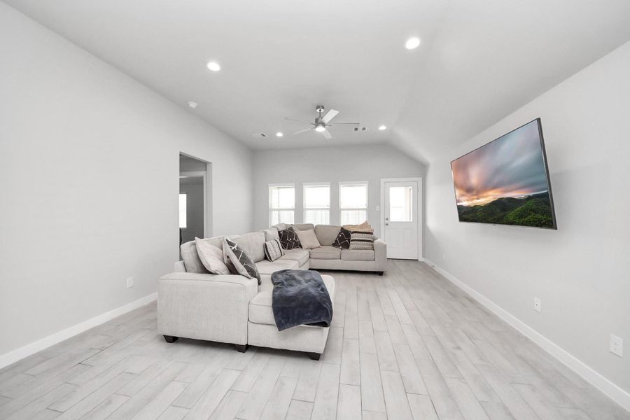 Spacious living room with high ceilings, recessed lighting, and large windows bringing in natural light. The entry to the left leads to the primary bedroom, while the door on the right provides access to the backyard.