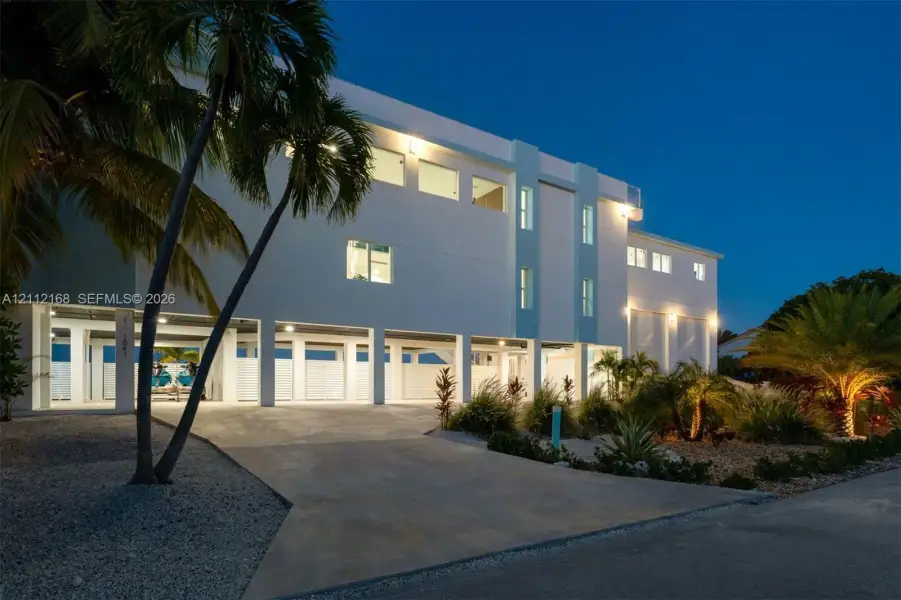 Multi-story exterior featuring a stilted foundation, concrete driveway, recessed ground-level parking, and native landscaping Multi-story exterior featuring a stilted foundation, concrete driveway, recessed ground-level parking, and native landscaping
