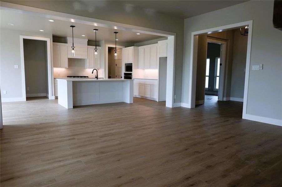 Kitchen featuring white cabinetry, an island with sink, stainless steel appliances, wood-type flooring, and decorative light fixtures