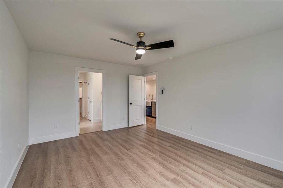 Unfurnished bedroom featuring ceiling fan, a sink, connected bathroom, wood finished floors, and baseboards