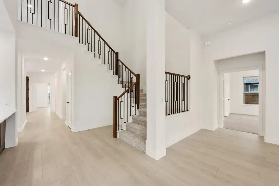 Open foyer with two-story staircase, wood and iron railing, and light hardwood floors Open foyer with two-story staircase, wood and iron railing, and light hardwood floors