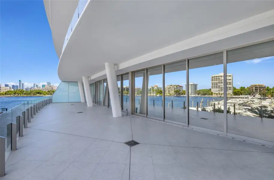 Expansive wraparound balcony featuring large-format tile flooring, a glass railing system, structural architectural pillars, and floor-to-ceiling glass wall panels