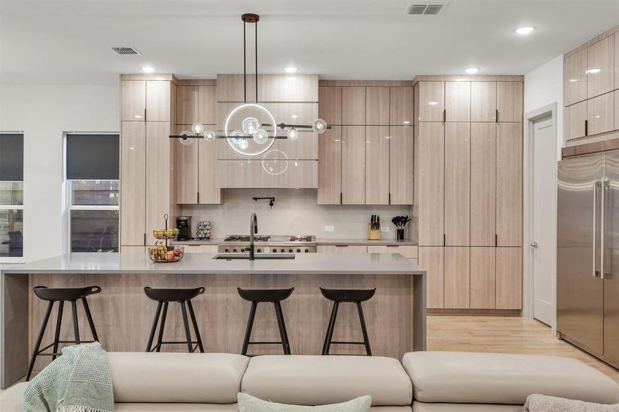 Kitchen featuring built in fridge, an island with sink, a breakfast bar area, light brown cabinetry, and hanging light fixtures