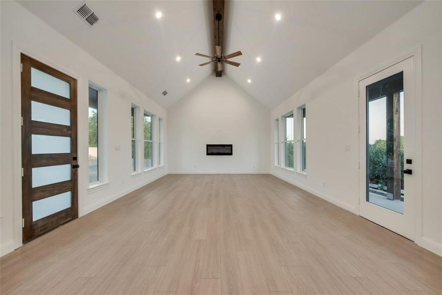Unfurnished living room featuring beamed ceiling, light wood-type flooring, recessed lighting, a glass covered fireplace, and a ceiling fan