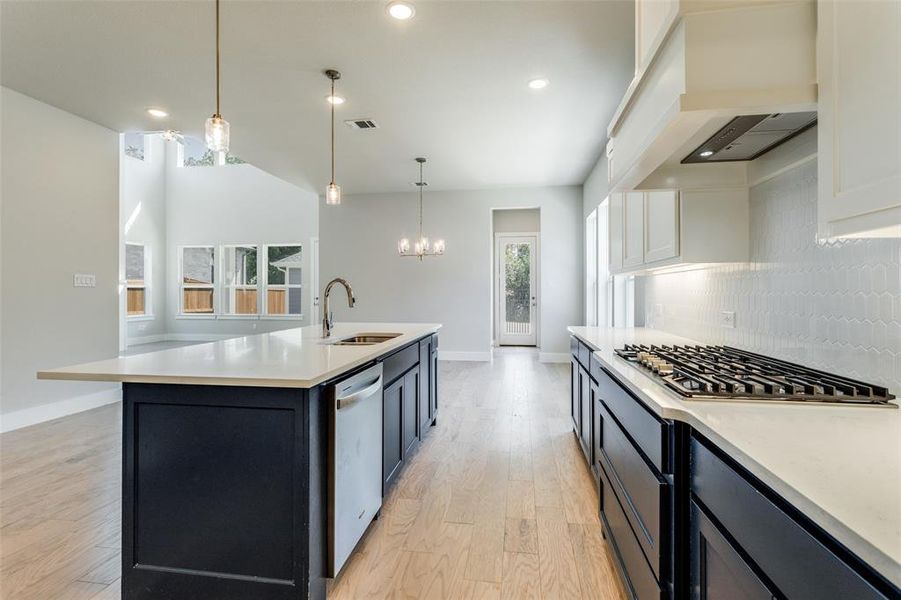 Kitchen with appliances with stainless steel finishes, light hardwood / wood-style floors, tasteful backsplash, sink, and an island with sink