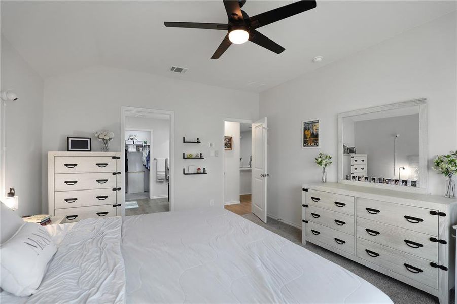 Bedroom with light colored carpet, ceiling fan, connected bathroom, and vaulted ceiling
