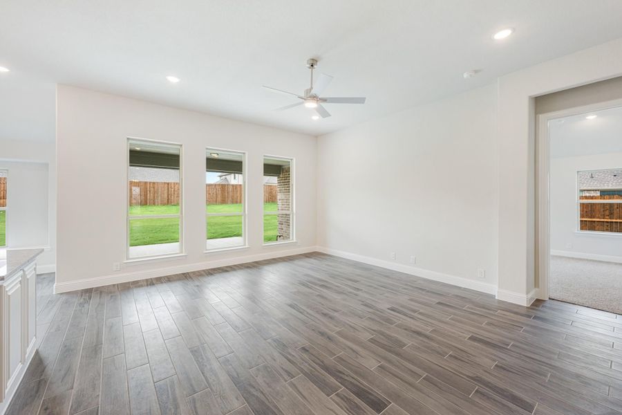 Open living room with gray wood-look tile floors, ceiling fan, and three backyard-facing windows