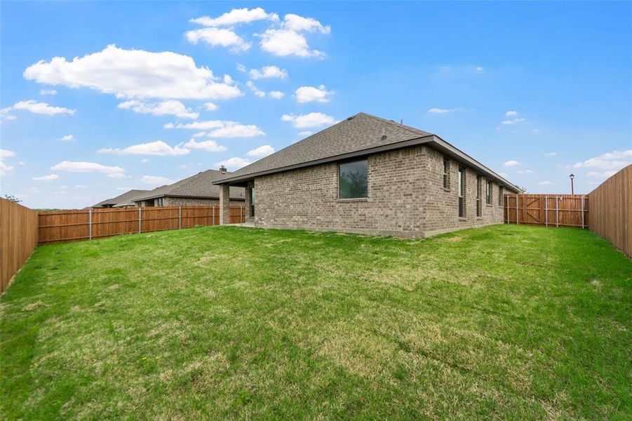 Expansive green lawn surrounded by a privacy fence, featuring a brick exterior and multiple windows