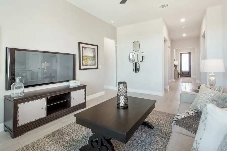 Living room with wall-mounted TV, dark wood media console, coffee table, and hallway leading to front door.
