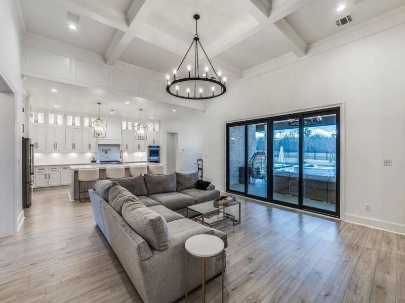 Living area with beamed ceiling, light wood-style floors, a chandelier, coffered ceiling, and a towering ceiling
