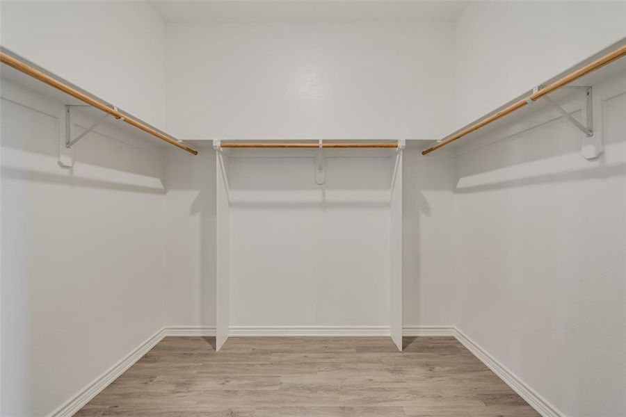 Walk in closet with light hardwood / wood-style floors