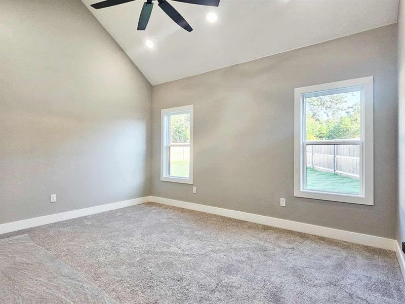 Primary bedroom w/ vaulted ceilings, ceiling fan, and carpet.