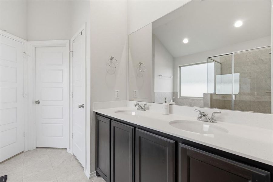 Full bath with double vanity, a shower stall, vaulted ceiling, and light tile patterned flooring