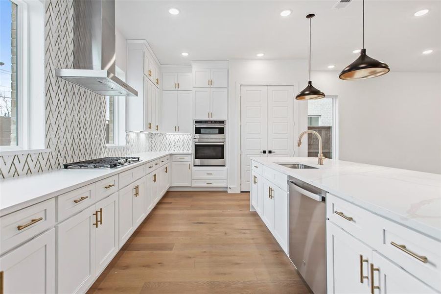 Kitchen with appliances with stainless steel finishes, pendant lighting, backsplash, light wood-type flooring, and wall chimney exhaust hood