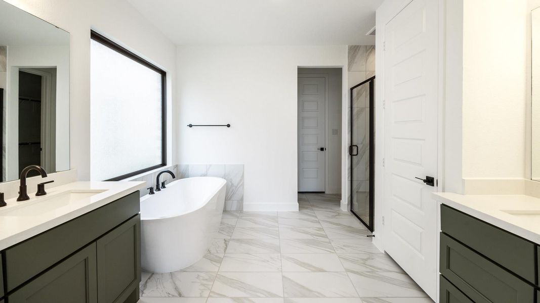 Bathroom featuring light marble finish flooring, two vanities, a freestanding bath, a shower stall, and a spacious closet