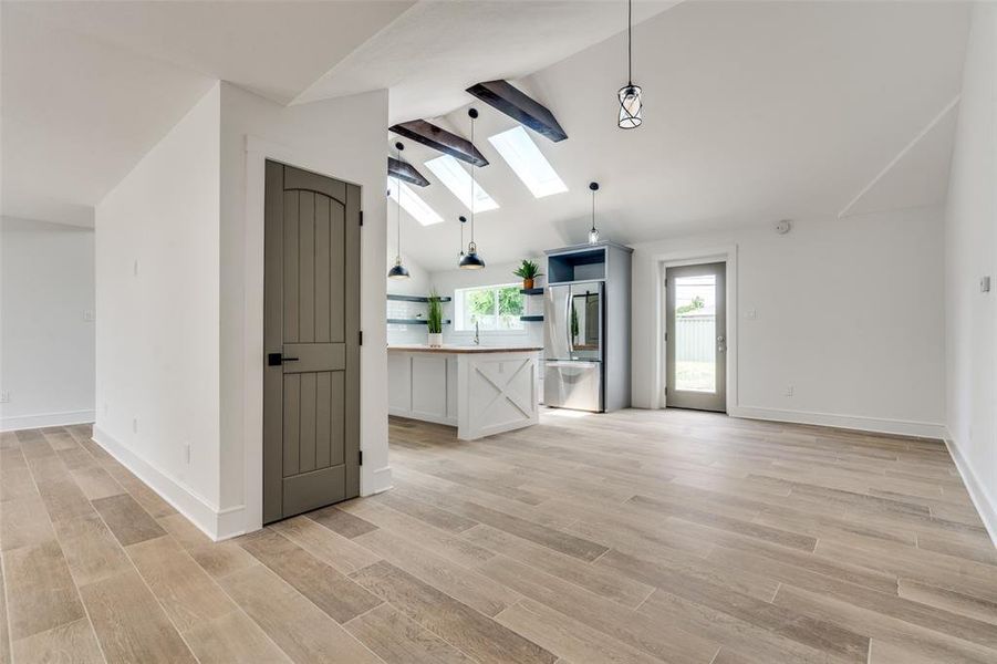 Open concept living area with high vaulted ceiling, beamed ceiling, light hardwood / wood-style flooring, and three skylights.