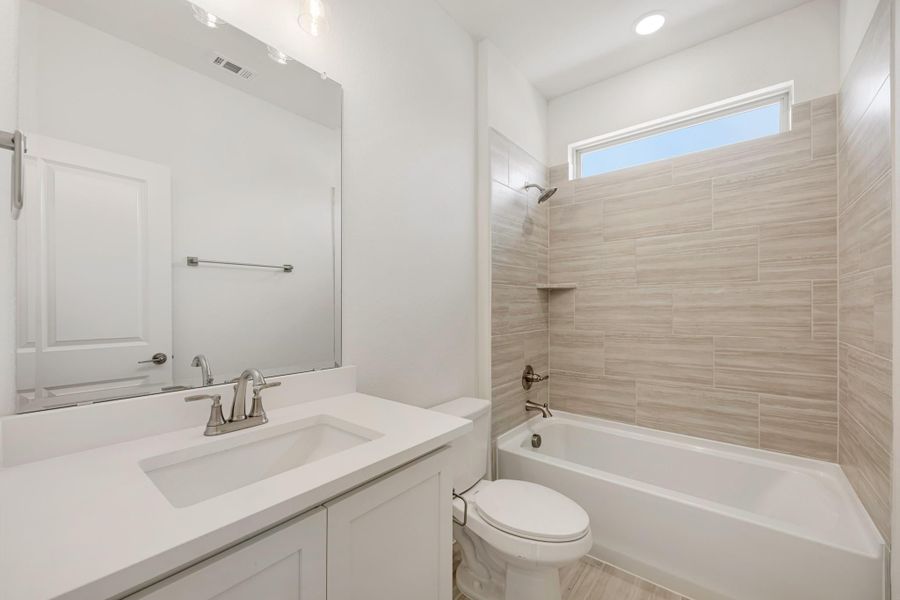 Bathroom with white vanity, large mirror, and tub-shower combo with beige tile surround
