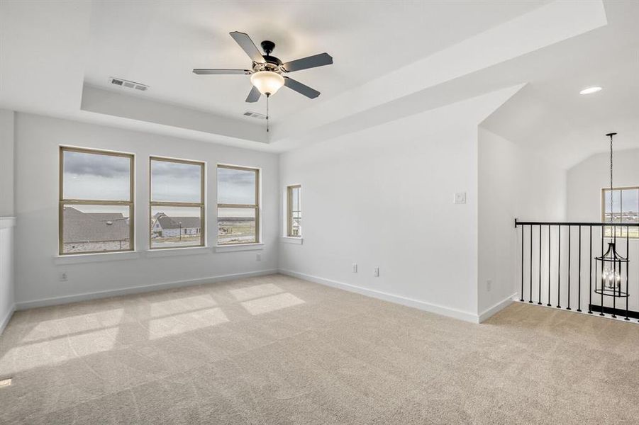 Unfurnished room featuring a tray ceiling, light colored carpet, ceiling fan, and suspended lighting