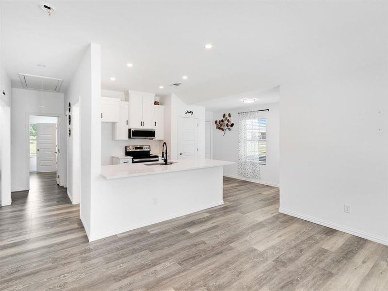 Open-concept kitchen and living area featuring wood-finish flooring, recessed lighting, white cabinetry, a kitchen island with sink, and black appliances