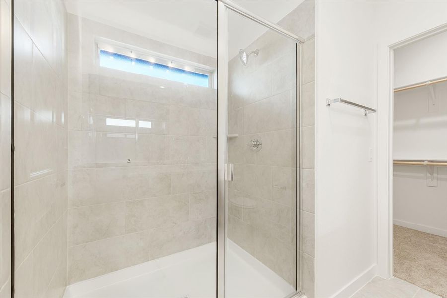 Walk-in shower with glass door and gray tile walls, next to a walk-in closet entrance