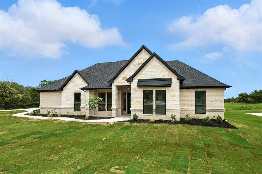 View of front of property with brick siding, a front lawn, roof with shingles, and stone siding