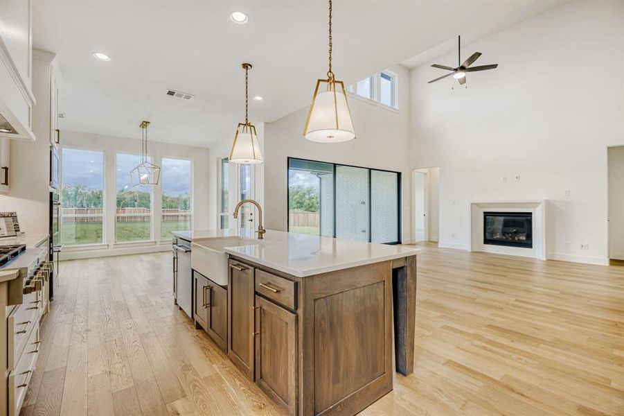 Kitchen featuring open floor plan, decorative light fixtures, light wood-type flooring, an island with sink, and a high ceiling